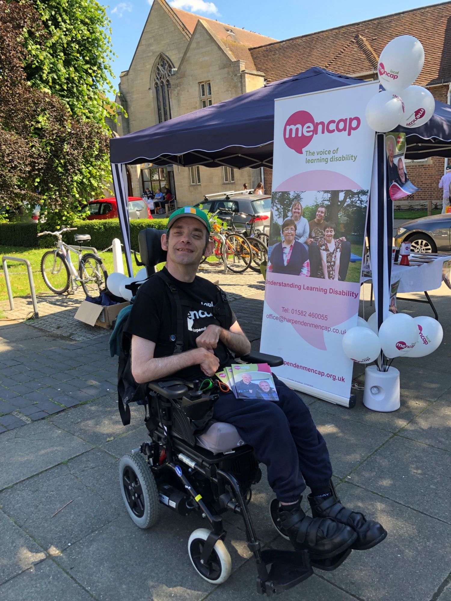 Man in wheelchair smiling near fundraising stall | Harpenden Mencap